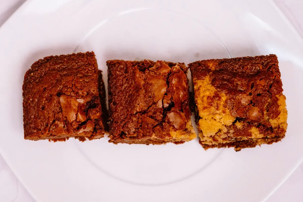 Trois carrés de brookie marbré, pâte à brownie et pâte à cookie mêlées, sur une assiette blanche