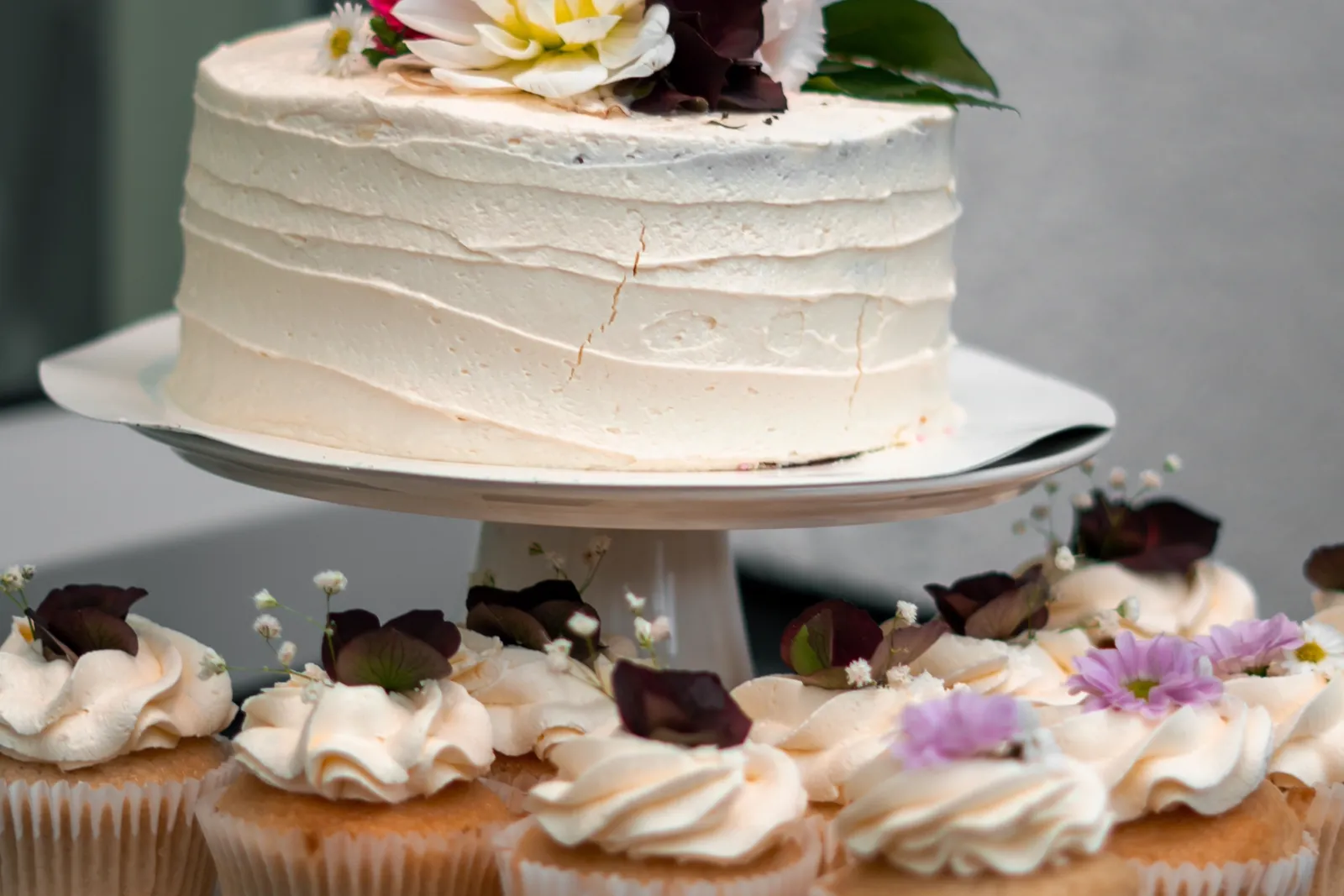 Gâteau rond à la crème décoré de fleurs fraîches, entouré de cupcakes