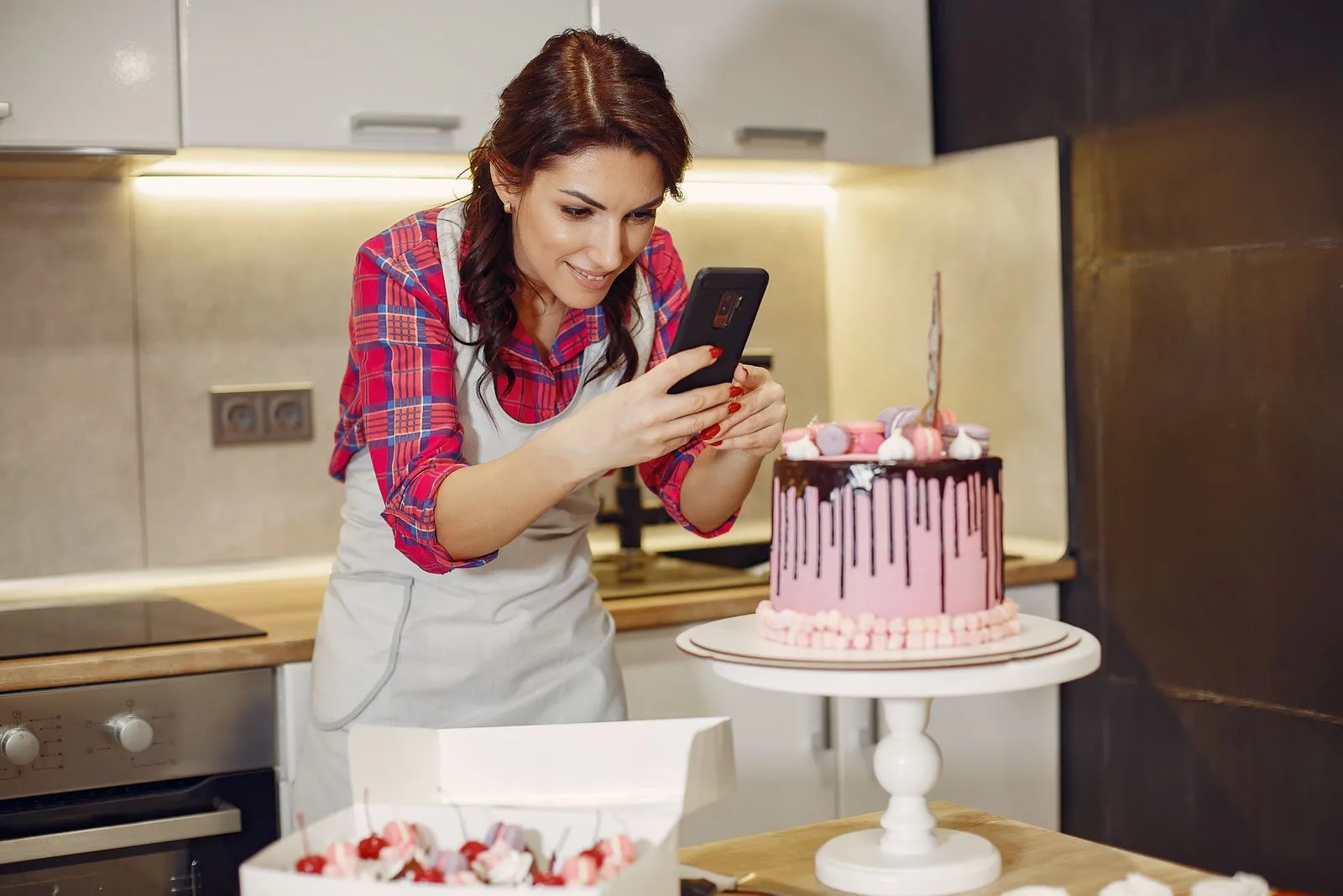 Pâtissière photographiant un gâteau avec son smartphone dans sa cuisine